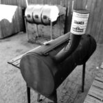 Black and white photo of outdoor barbecue grills and smokers in a fenced yard.